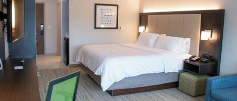 A hotel room with a bed, bedside table, lamp, TV, and a chair.