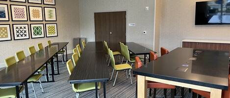 A conference room with a long table, multiple chairs, framed artwork on the wall, and a television screen.