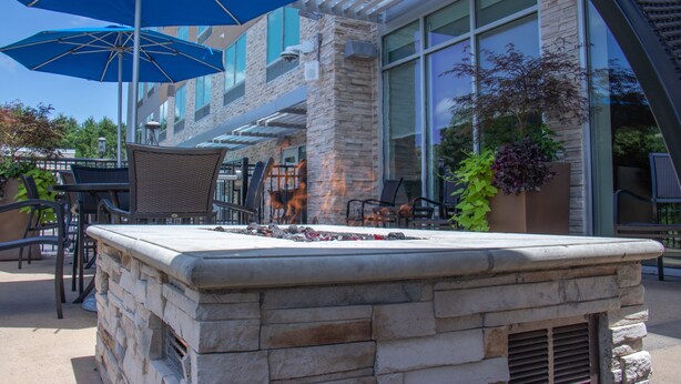 An outdoor seating area with stone tables, blue umbrellas, and potted plants. - Holiday Inn Express & Suites Tuscaloosa East - Cottondale by IHG (Cottondale)