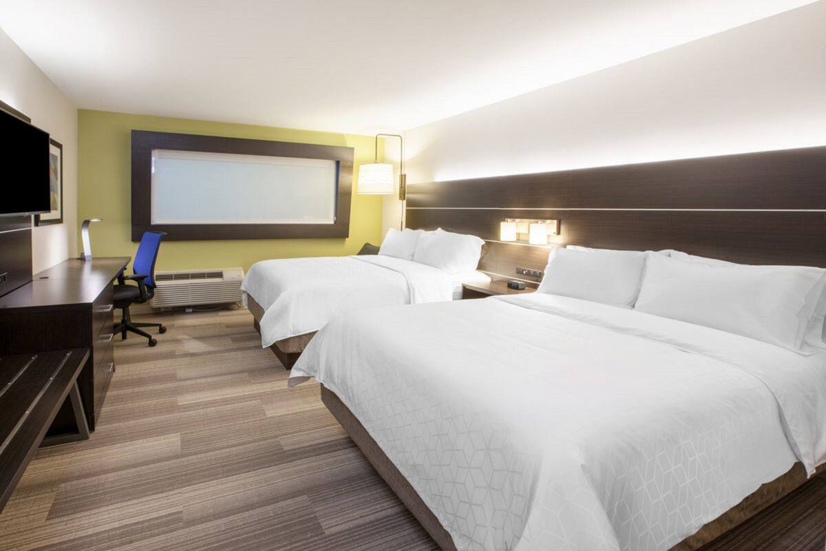 A hotel room with two beds, a desk, a chair, a TV, and a large window.