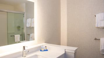 Un baño moderno con un espejo grande, un lavabo blanco y una cabina de ducha con paredes de vidrio.