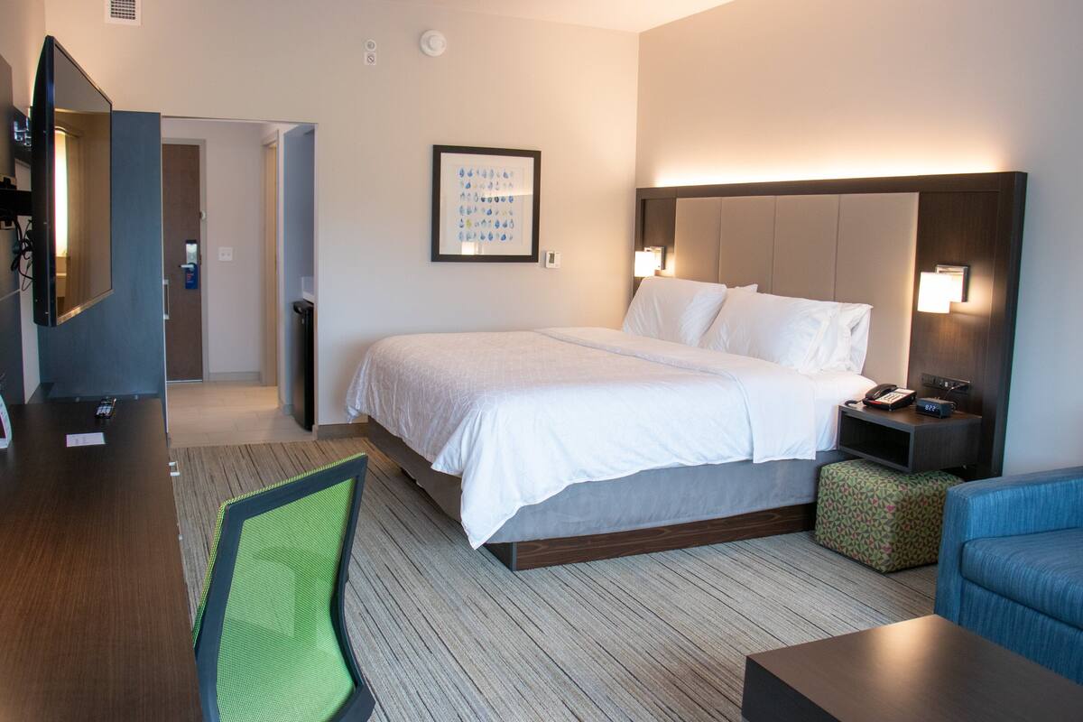 A hotel room with a bed, bedside table, lamp, TV, and a chair.