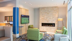 A modern lounge area with a flat-screen TV, comfortable seating, a fireplace, and a patterned carpet. - Holiday Inn Express & Suites Tuscaloosa East - Cottondale by IHG (Cottondale)
