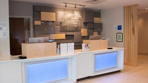 A reception desk with a modern design, featuring a neutral color palette and a combination of wood and metal elements. - Holiday Inn Express & Suites Tuscaloosa East - Cottondale by IHG (Cottondale)