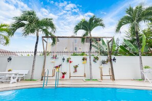 A swimming pool with a pergola, palm trees, and a white wall with hanging plants. - Diamond Sea Villa (Ho Chi Minh City)