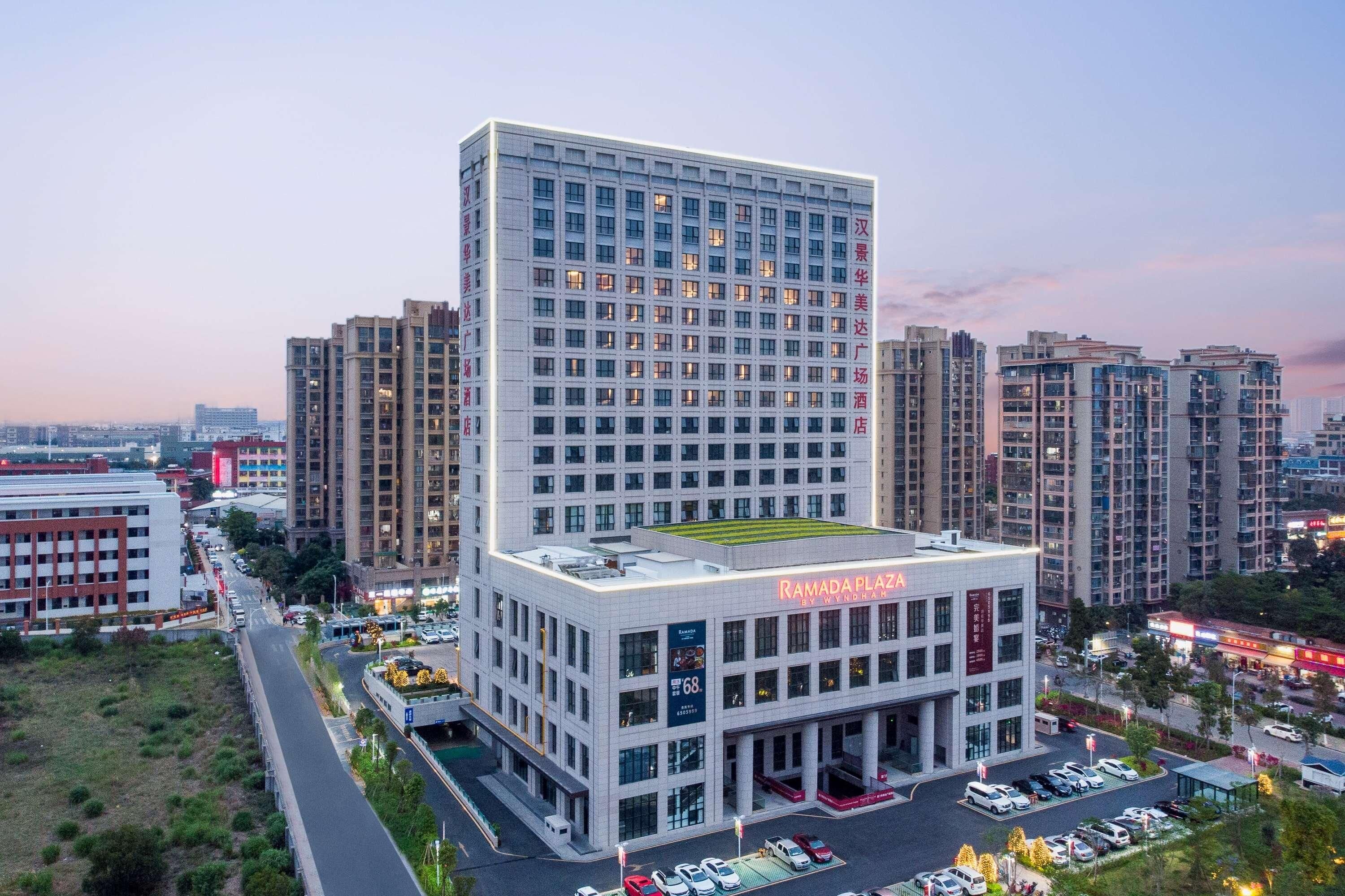 A modern hotel building with multiple floors, a rooftop terrace, and a parking area.