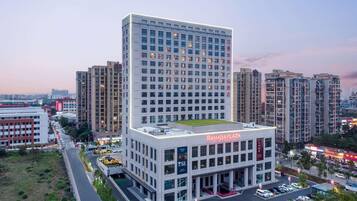 A modern hotel building with multiple floors, a rooftop terrace, and a parking area.