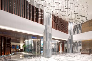 En rummelig lobby med høje lofter, en marmorbelægning og moderne arkitektoniske detaljer, herunder et karakteristisk bølget loftdesign og store søjler.