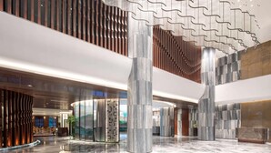 Un hall amplio con techos altos, suelo de mármol y elementos arquitectónicos modernos, incluyendo un diseño de techo ondulado y grandes pilares.