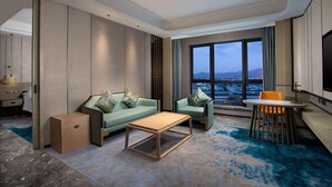 Una habitación de hotel moderna con sofá, una mesa de centro, una mesa de comedor con sillas y un ventanal con vistas a la ciudad.