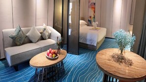 Una habitación de hotel con sofá, cama, mesa de comedor con fruta y una mesita con una planta.