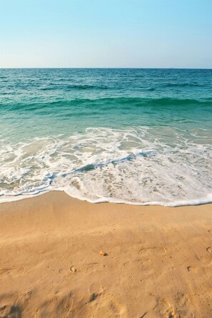 Een strand met helder water, een zandstrand en voetsporen.
