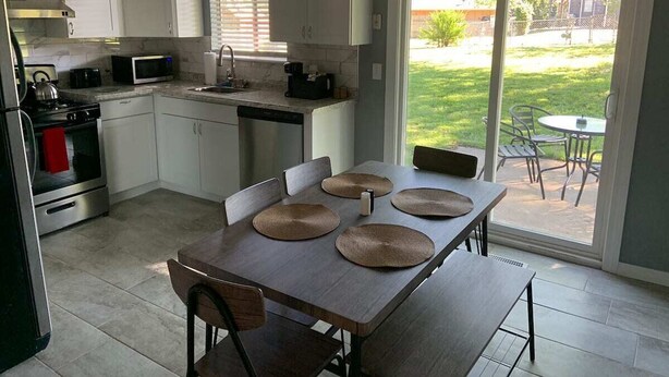 Una cocina moderna con armarios blancos, una estufa de acero inoxidable y un comedor con mesa y sillas.