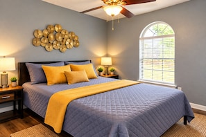 A bedroom with a bed, nightstands, a wall clock, a ceiling fan, and a window with blinds.