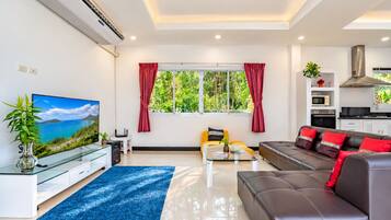 A modern living room with a sofa, a coffee table, a TV, and a kitchen area.