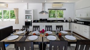 A modern kitchen with white cabinets, a central island, and a dining area set for six. - 4 Br Private Pool Villa GA (Chalong)