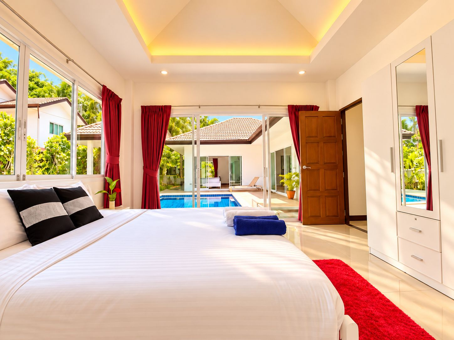 Une chambre dotée d’un grand lit, offrant une vue sur une piscine et donnant accès à un balcon par une porte.