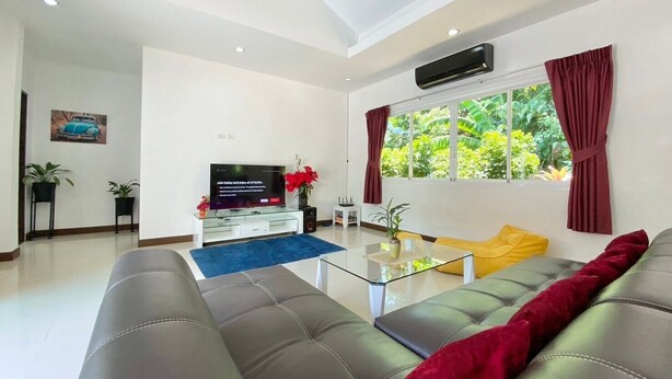 A modern living room with a sofa, TV, and a window with curtains. - 4 Br Private Pool Villa GA (Chalong)