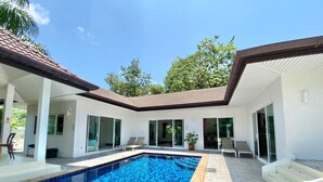 Una casa moderna con piscina, puertas de cristal amplias y techo de tejas.