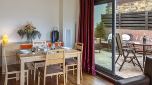 A dining area with a wooden table set for four, chairs, a vase of flowers, and a view of the outdoor patio through a glass door.