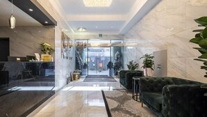 A modern lobby with marble floors, a reception desk, green upholstered seating, and a chandelier.