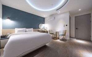 Una habitación de hotel moderna con una cama grande, mesitas de noche y una mesa redonda con sillas.