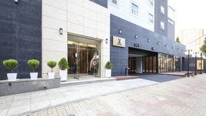 A modern hotel entrance with a glass door, potted plants, and a sign indicating the hotel name.