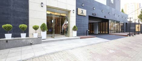 A modern hotel entrance with a glass door, potted plants, and a sign indicating the hotel name.