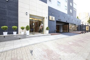Una entrada de hotel moderna con puerta de vidrio, plantas en macetas y un cartel con el nombre del hotel.
