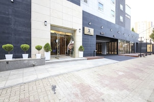 Una entrada de hotel moderna con puerta de vidrio, plantas en macetas y un cartel con el nombre del hotel.