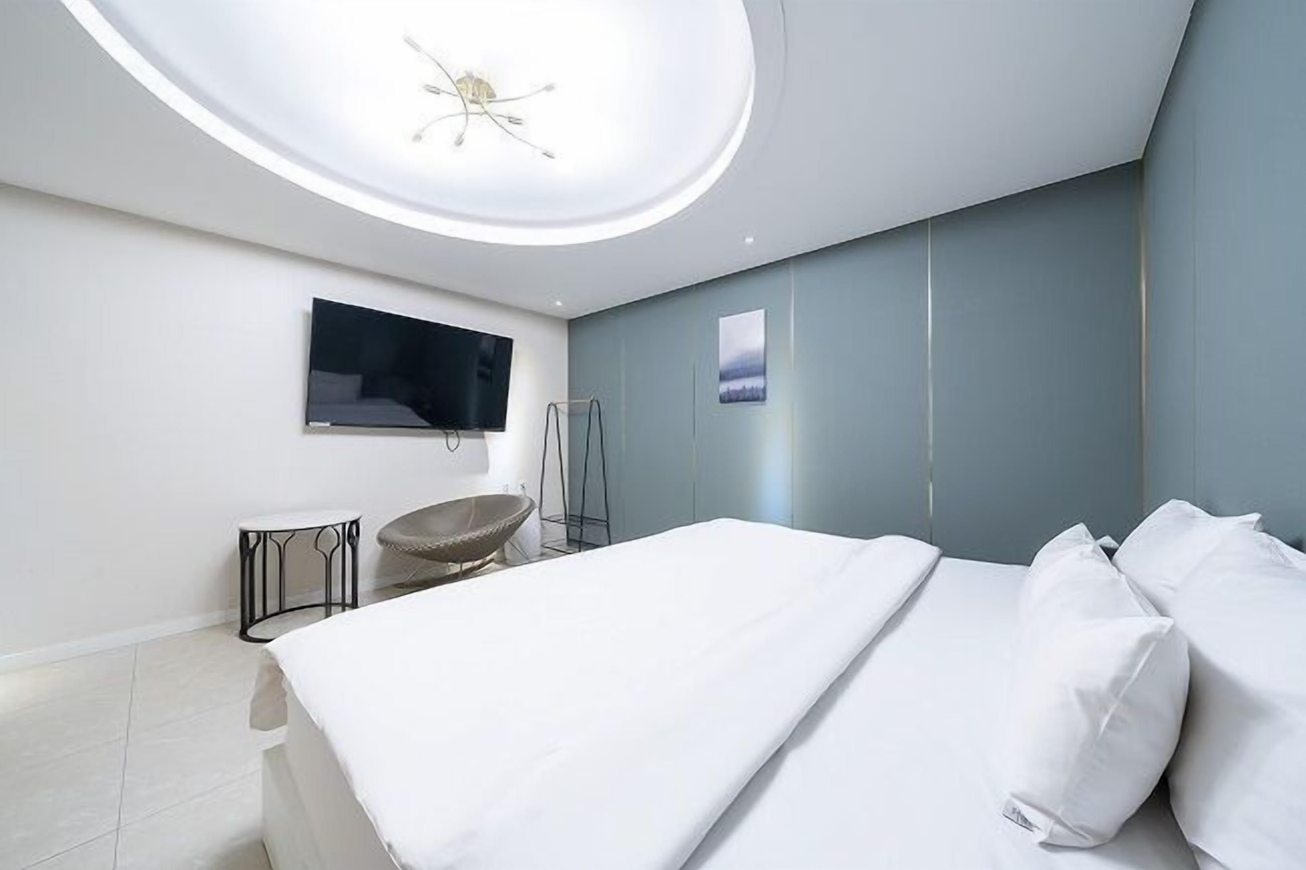 A modern bedroom with a bed, a television, a circular ceiling light, and a small table.