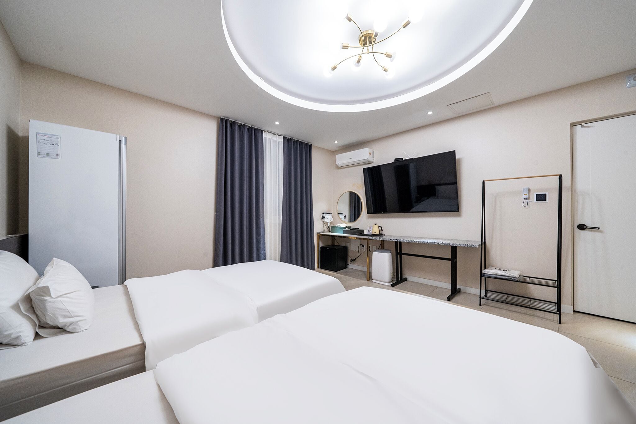 A hotel room with two beds, a desk with a computer, a flat-screen TV, a mirror, and a wardrobe.