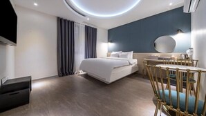 Una habitación de hotel moderna con una cama, mesita de noche, silla y un espejo redondo.
