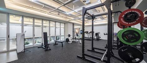 A gym with weightlifting equipment, benches, and a large window providing natural light.