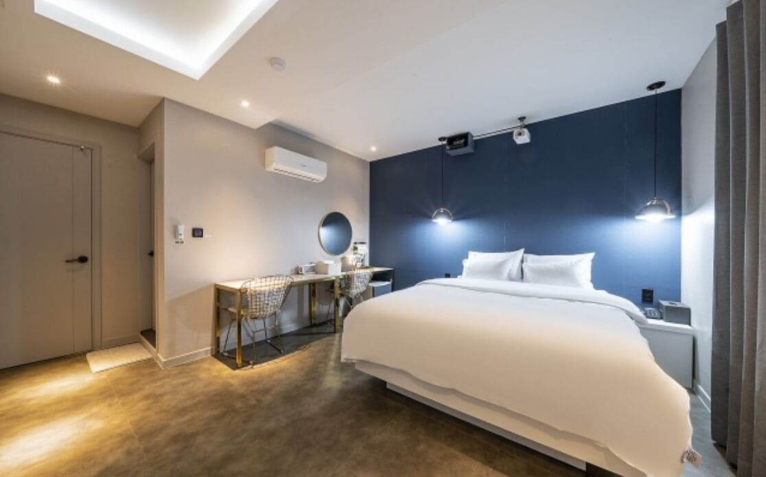 Een moderne hotelkamer met een groot bed, een bureau met stoel, een ronde spiegel en een donkere accentmuur.