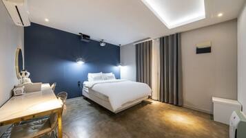 A modern hotel room with a bed, bedside table, and a desk with a chair.