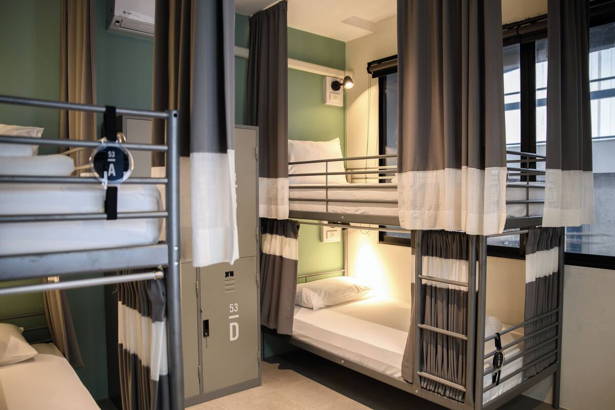 A bunk room with two beds, a wardrobe, and a window with curtains.