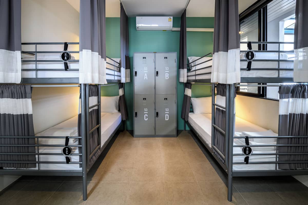 A dormitory room with bunk beds, a wardrobe, and an air conditioning unit.
