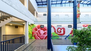 A multi-level atrium with a staircase, a mural with large floral designs, and a blue railing. - Stay Wanglang (Bangkok)