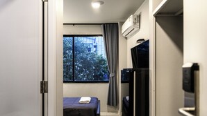 A small bedroom with a bed, a window with curtains, an air conditioning unit, and a television. - Stay Wanglang (Bangkok)