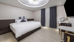 Una camera d'albergo moderna con un letto grande, una lampada a soffitto rotonda, un'area pranzo con tavolo e sedie, e una TV a schermo piatto montata a parete.