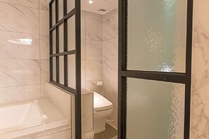 A modern bathroom with a bathtub, toilet, and glass shower enclosure. - Hotel KNOX (Cheonan)