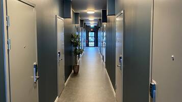 A long, narrow hallway with doors on both sides, leading to a bright exit at the end.