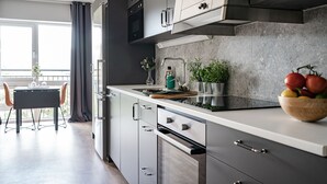 A modern kitchen with grey cabinets, a stainless steel range hood, and a wooden cutting board with a bowl of fruit. - Magnolia House Norrviken (Sollentuna)