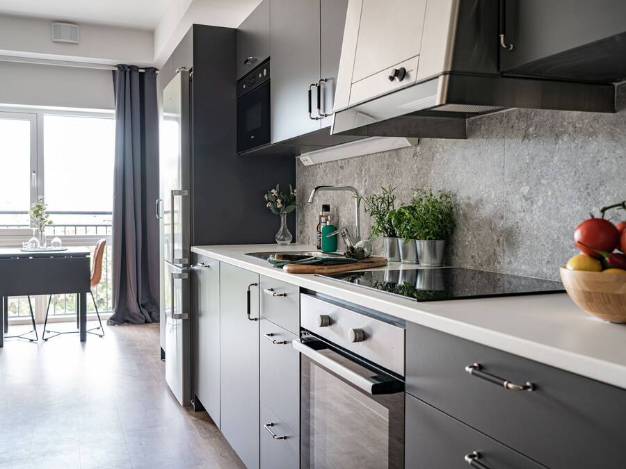 Una cocina moderna con armarios grises, una campana extractora de acero inoxidable y una tabla de cortar de madera con un bol de fruta.