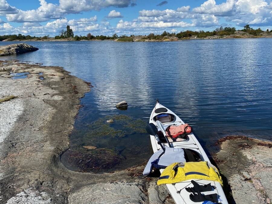 A kayak resting on a rocky shore with a clear view of a lake and distant trees under a partly cloudy sky.