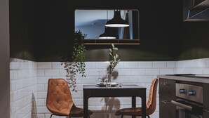 A modern kitchen with a dining table, two chairs, a hanging pendant light, and a built-in oven. - Magnolia House Norrviken (Sollentuna)