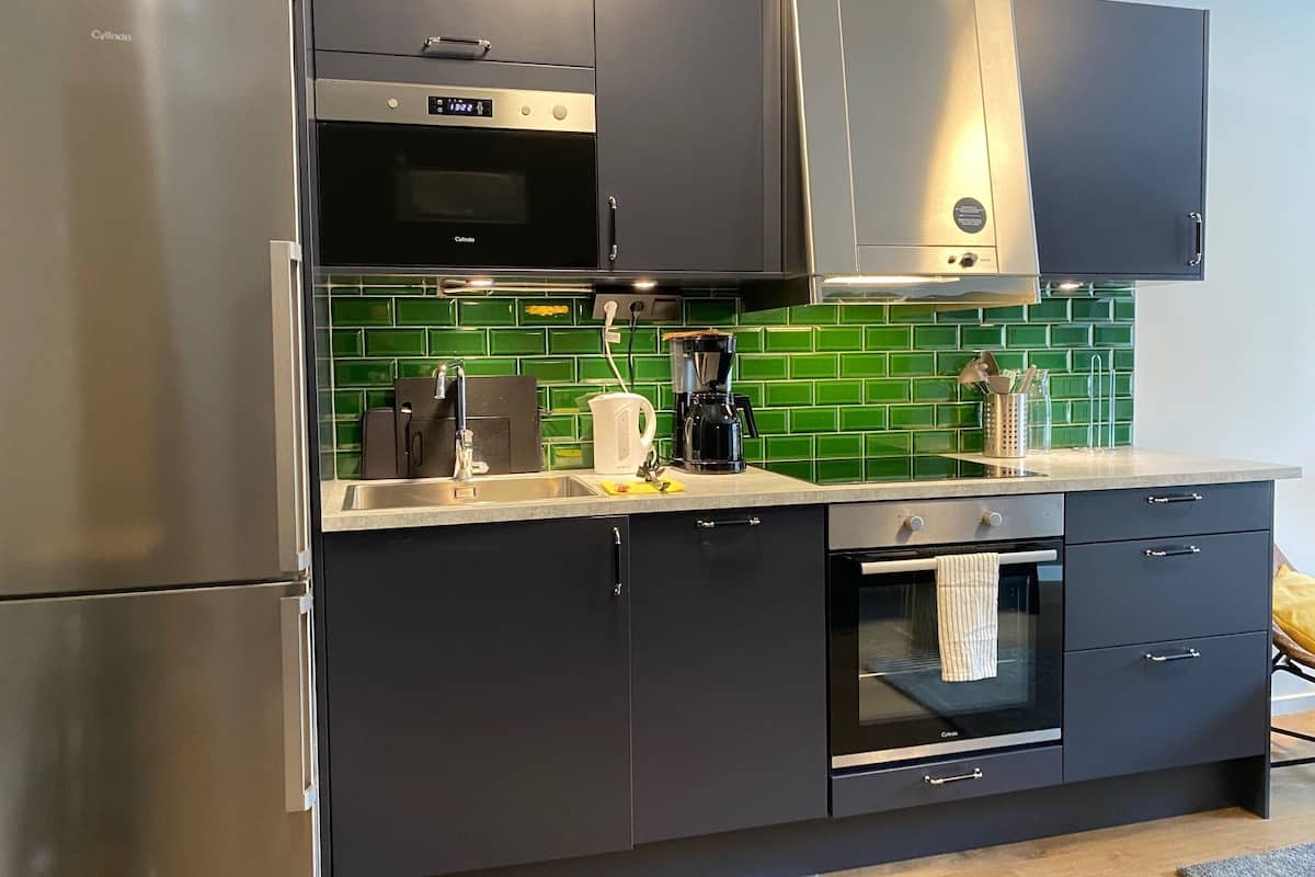 Una cocina moderna con electrodomésticos de acero inoxidable, cafetera y salpicadero de azulejos verdes.