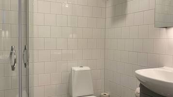 A modern bathroom with white tiled walls, a glass shower enclosure, a white toilet, a towel rack, and a sink with a mirror above it.