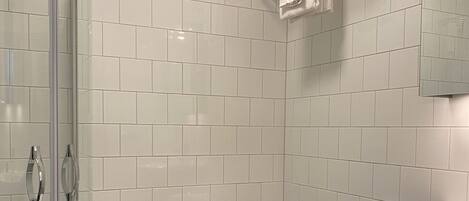 A modern bathroom with white tiled walls, a glass shower enclosure, a white toilet, a towel rack, and a sink with a mirror above it.